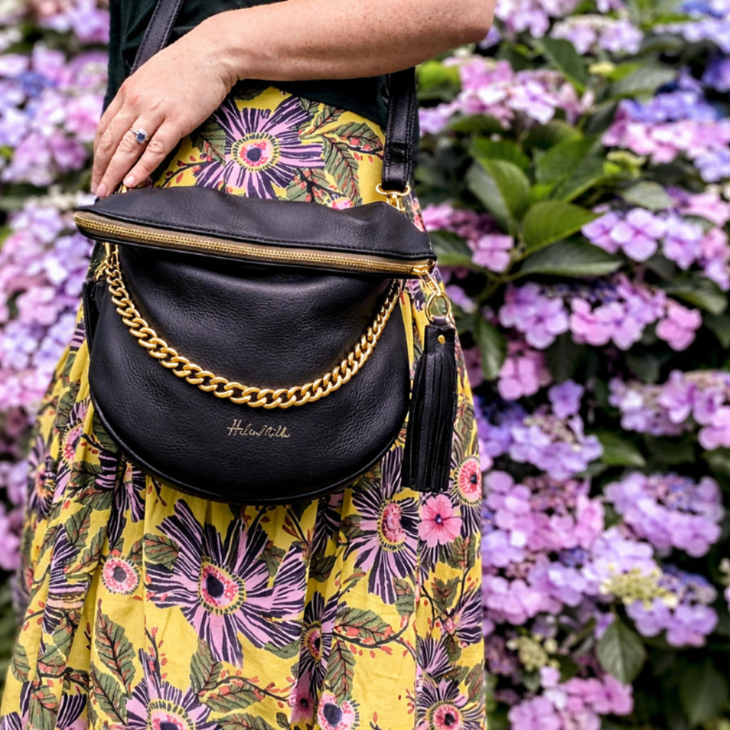 Person holding a black handbag with floral dress and purple flowers in the background